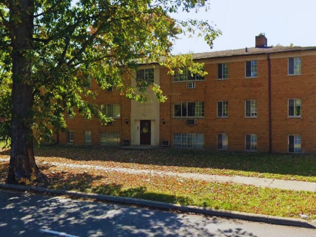Brick apartment building with tree and sidewalk.