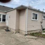 Small beige house with concrete driveway.