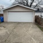 Detached garage with concrete driveway and trees.