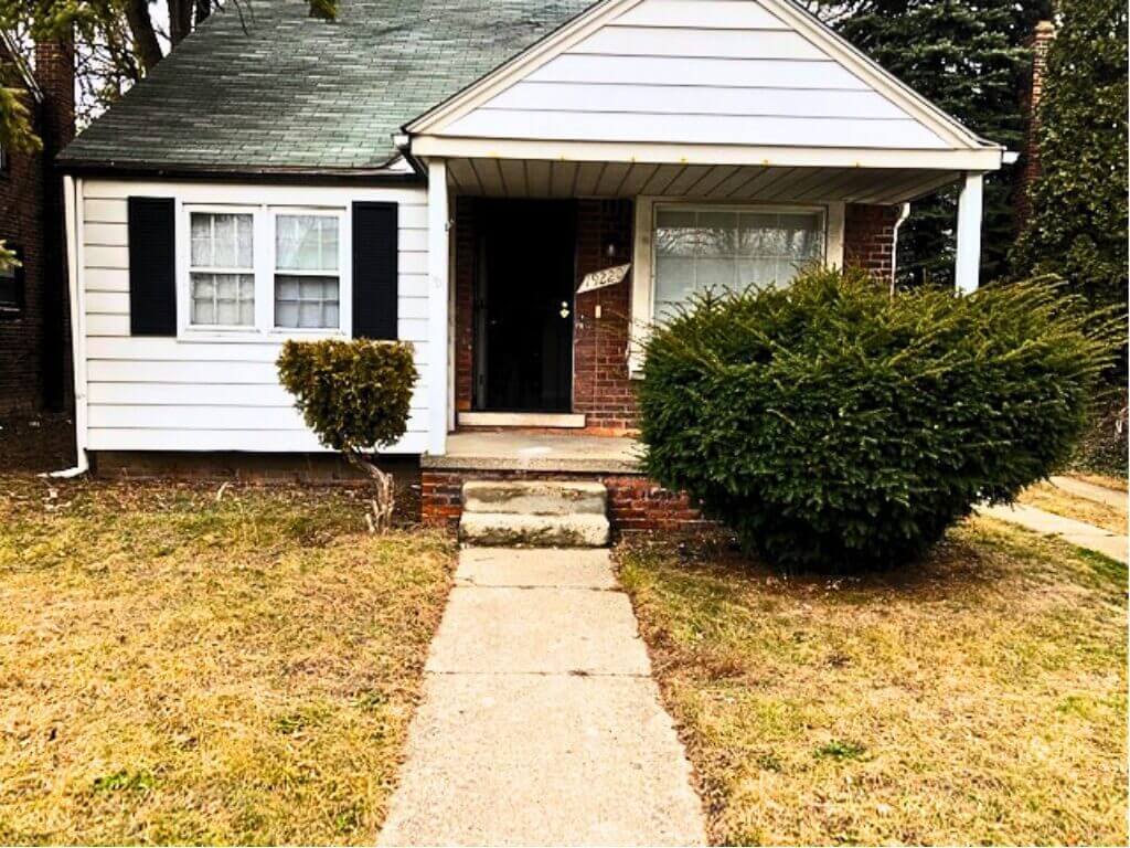 Small house with front porch and bushes.