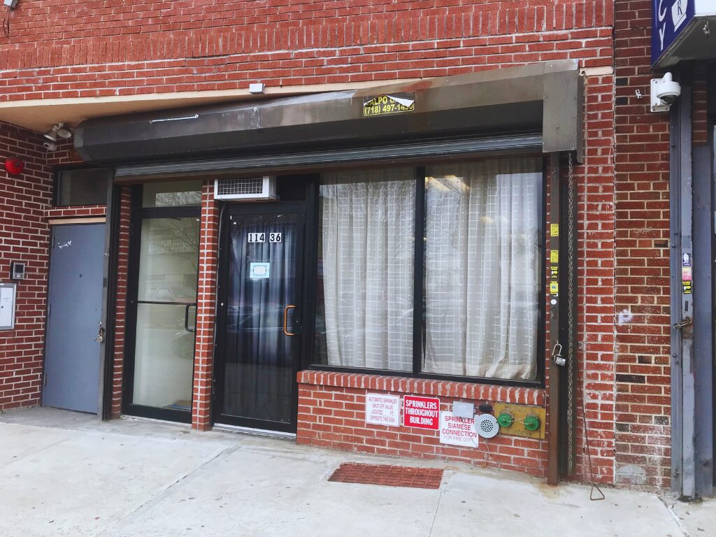 Red brick storefront with closed metal gate.